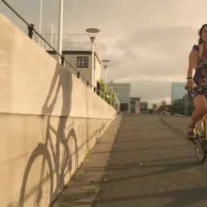 A woman rides a bicycle along Bristol Harbourside at sunset in a scene from a Sustrans film produced by Floating Harbour