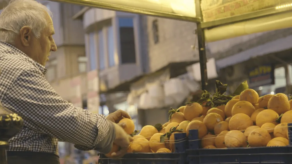 An older man arranges oranges at an evening market stall in Killis, captured during Floating Harbour’s Judo for the World project while working in a red zone environment.