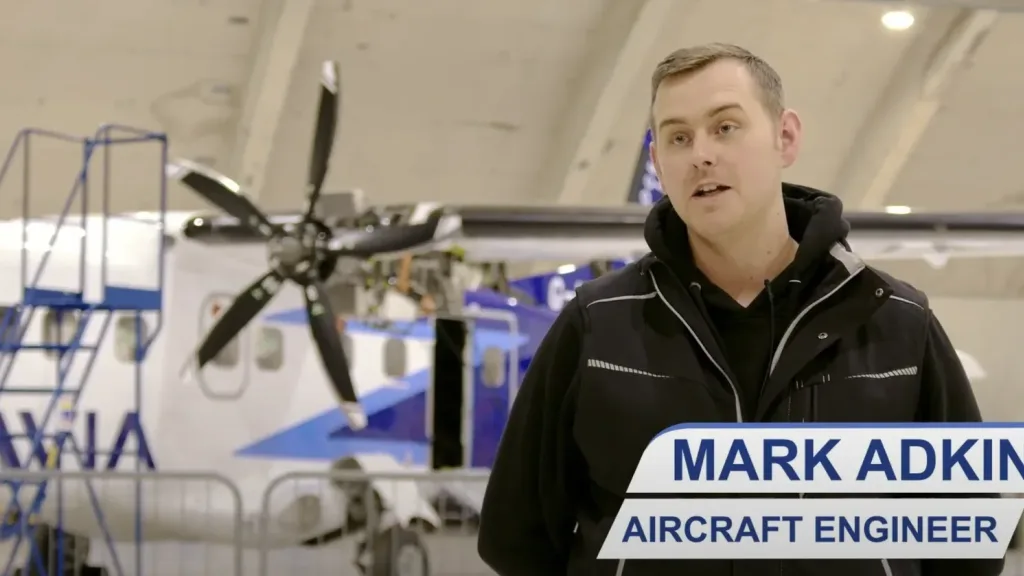 An aircraft engineer speaks in a hangar with a ZeroAvia plane behind him