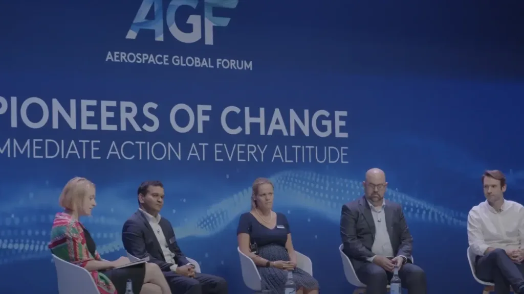 Panel of speakers sit on stage in front of a blue Aerospace Global Forum backdrop