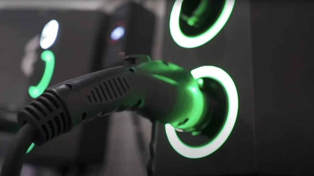 Close up of an electric vehicle charging plug with green LED light around the socket.