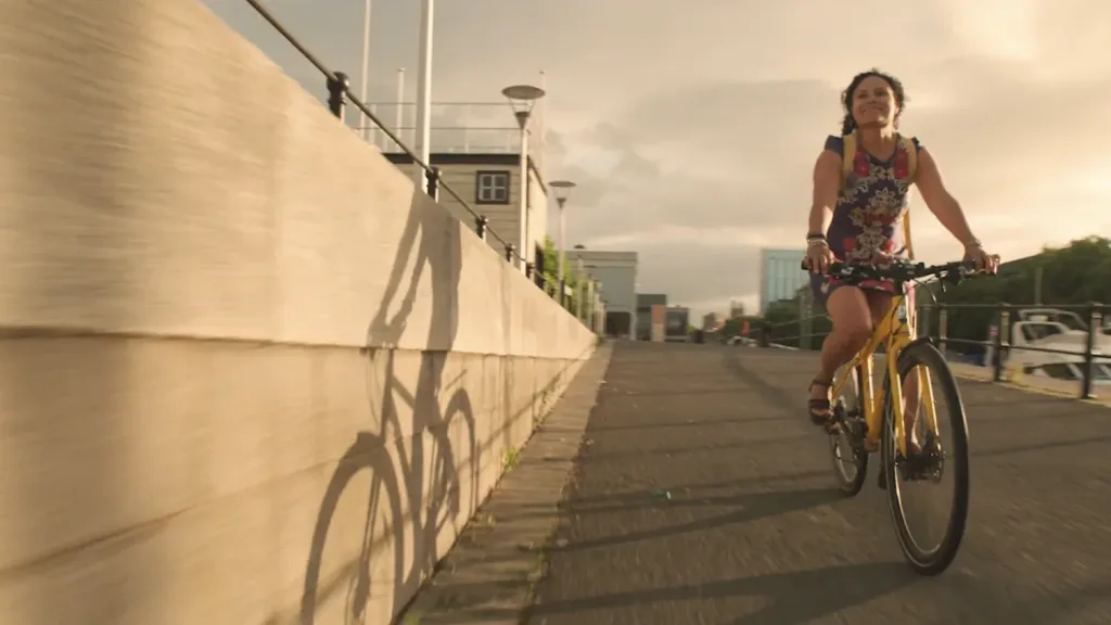 A woman rides a bicycle along Bristol Harbourside at sunset in a scene from a Sustrans film produced by Floating Harbour