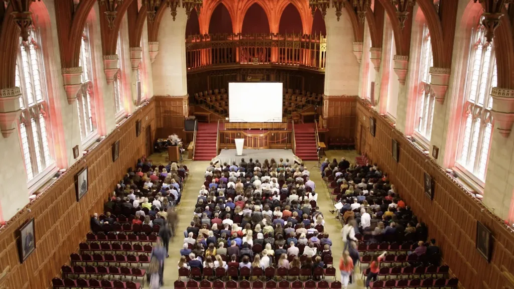 Large audience inside a grand hall at the University of Bristol watching a presentation on a central screen.