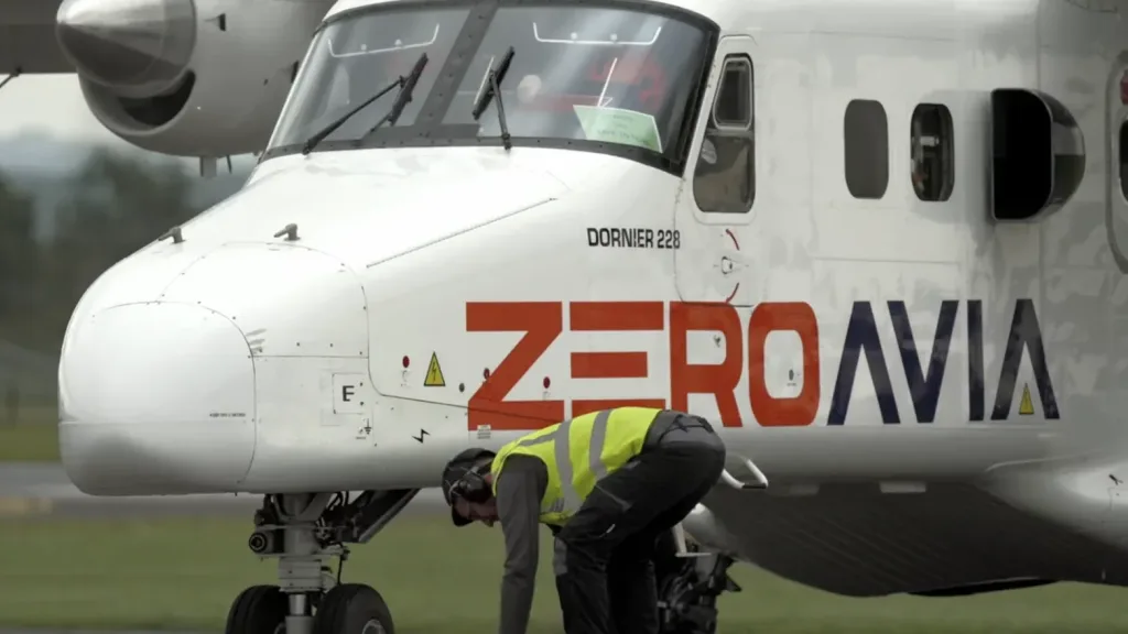 ZeroAvia branded Dornier 228 aircraft with a ground crew member working beneath the nose on a runway