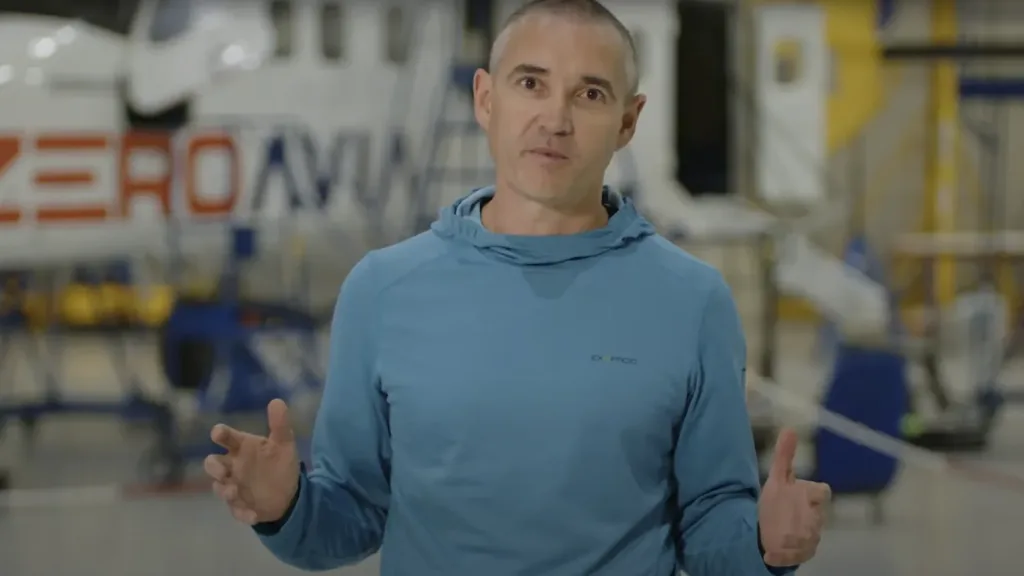 CEO of ZeroAvia speaking during an interview inside the company’s aircraft hangar, with ZeroAvia branding visible on the hydrogen-electric aircraft in the background.