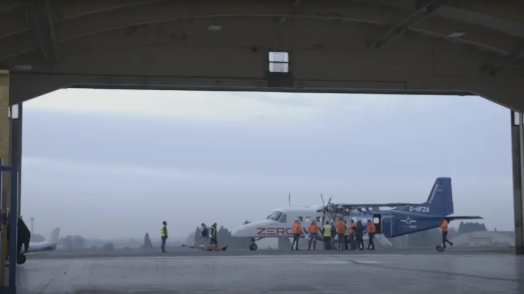 ZeroAvia hydrogen-electric Dornier 228 on the airfield apron with engineering crew preparing the aircraft for a test flight, seen from inside the hangar.