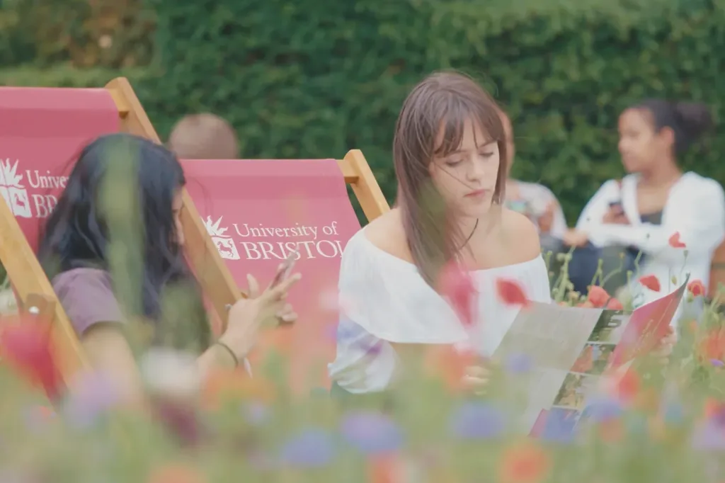 Students sit on University of Bristol deckchairs in a garden reading and chatting amongst flowers