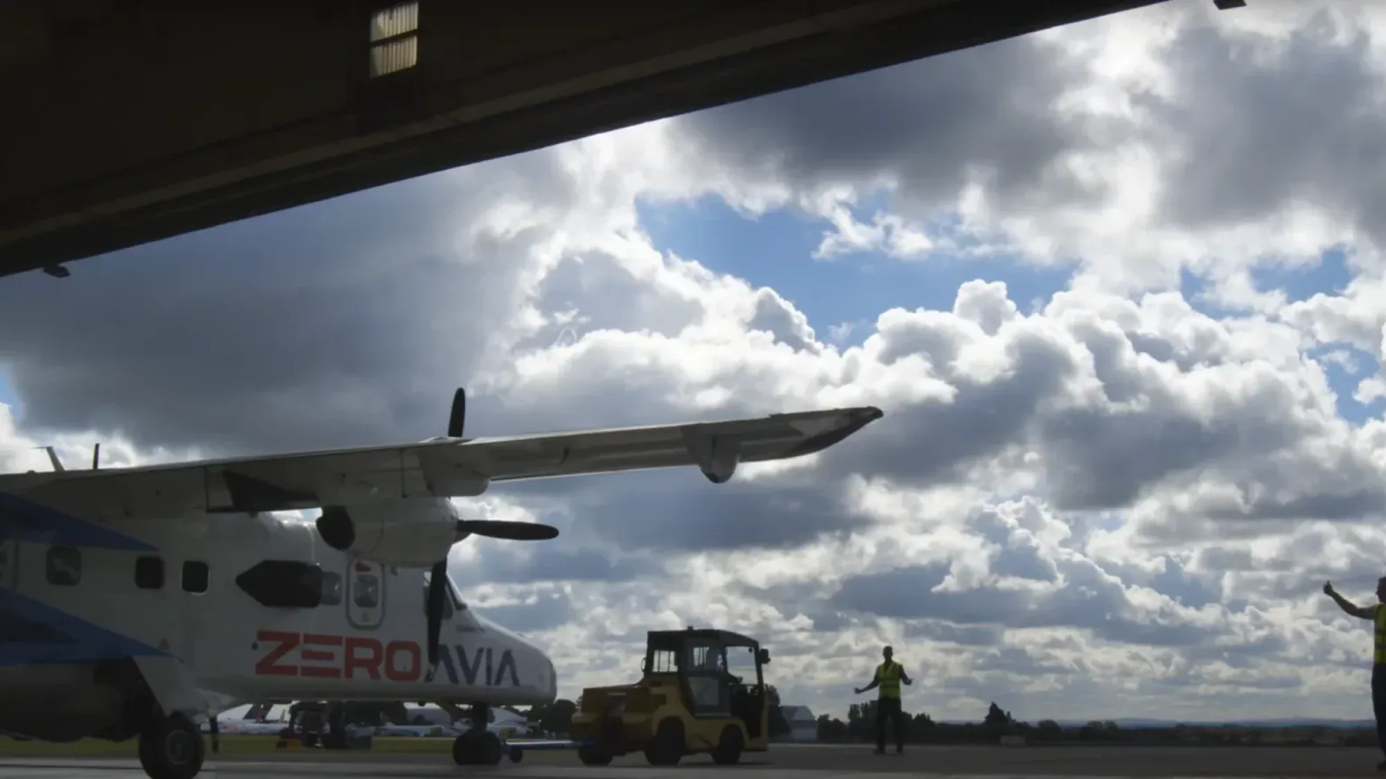 Silhouette of the ZeroAvia Dornier 228 aircraft being manoeuvred out of a hangar under dramatic cloudy skies, filmed by Floating Harbour.