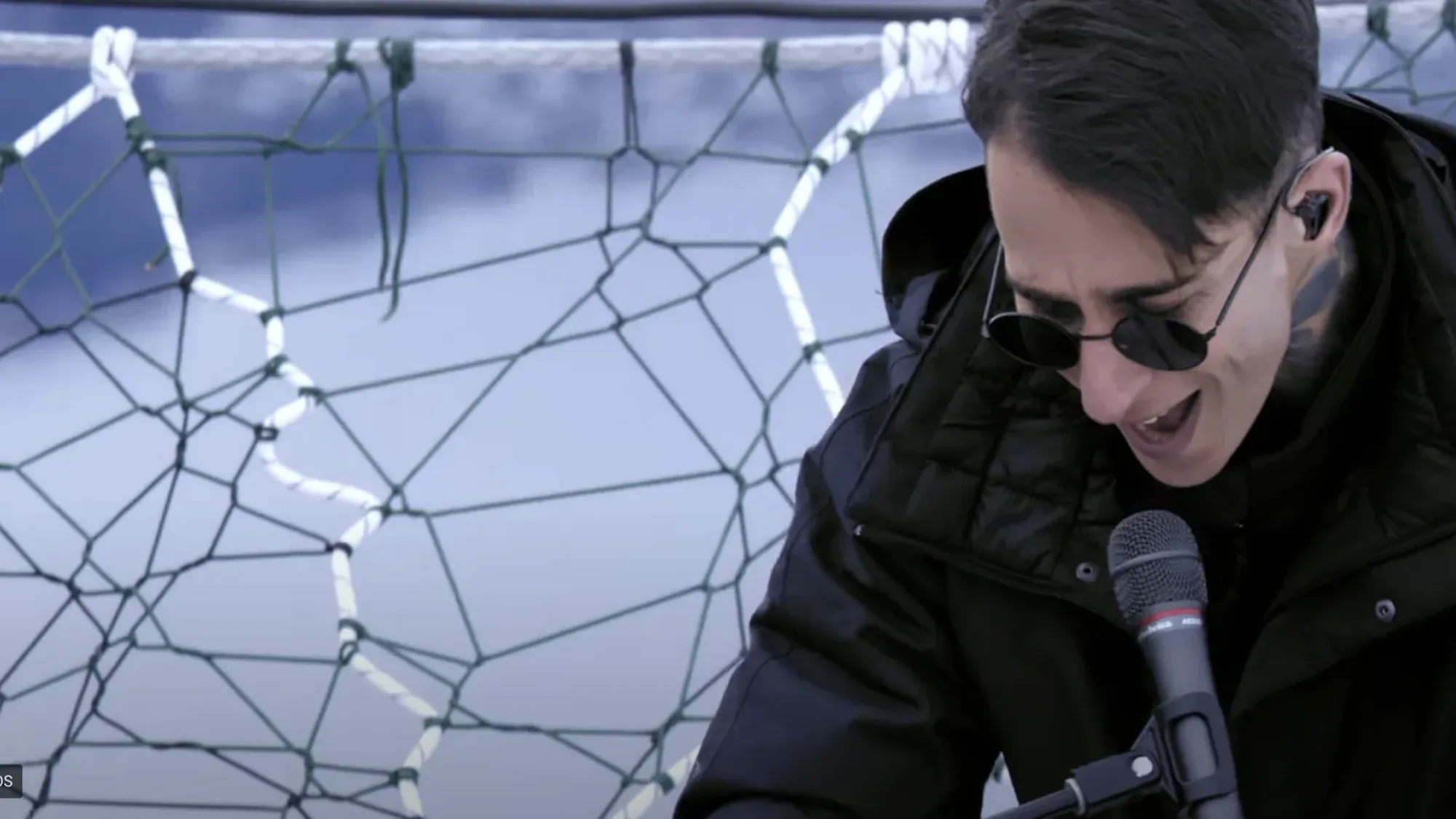 Music performer singing into a microphone outdoors in cold conditions with netting behind