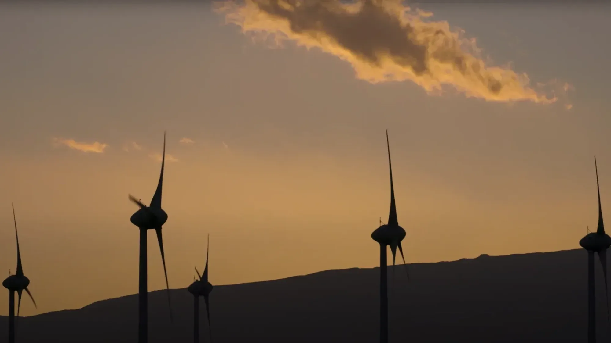Silhouetted wind turbines turning against a sunset sky with clouds