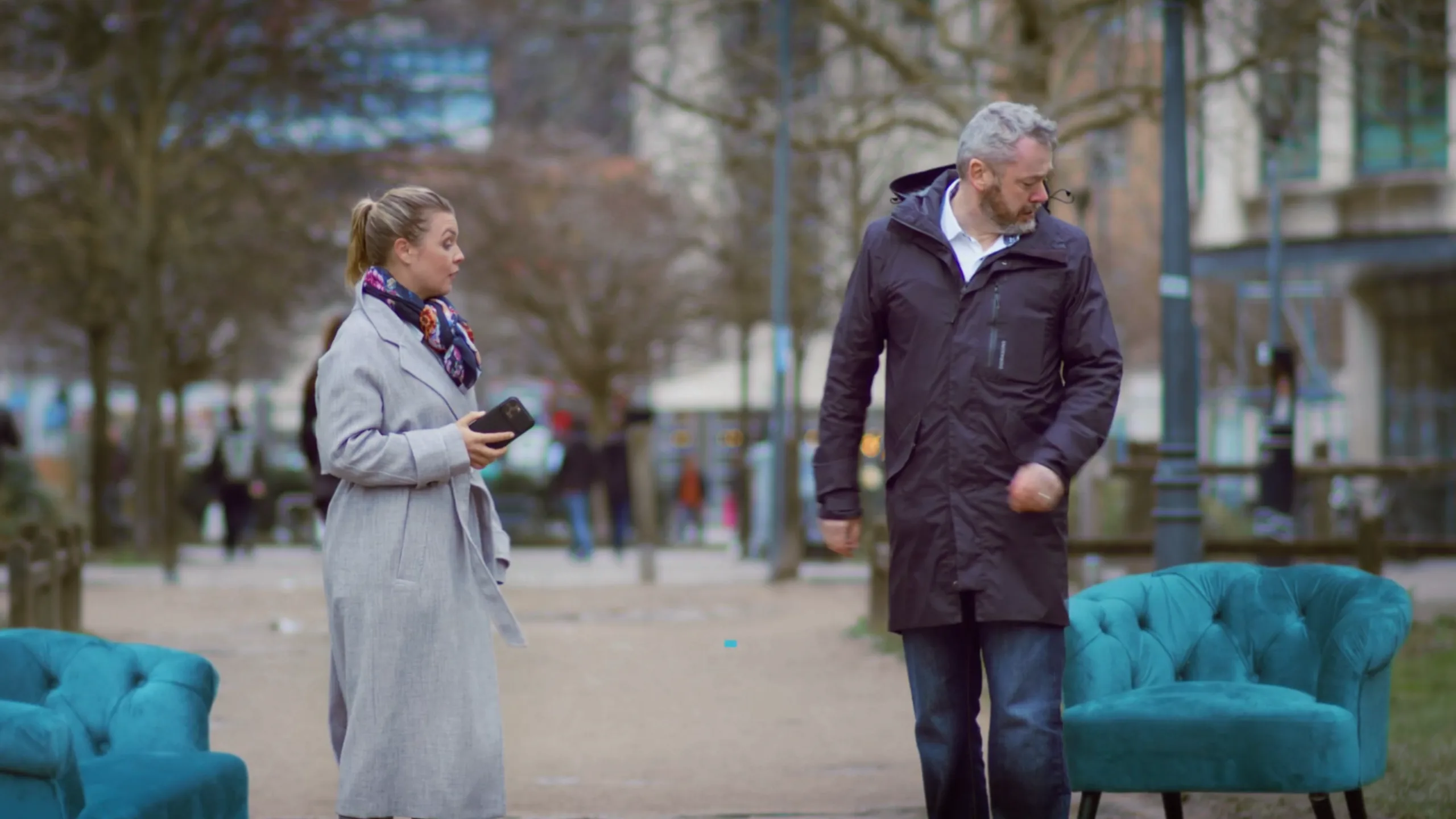 A man and woman react as a teal chair unexpectedly falls from the sky while the woman stops to help him, filmed by Floating Harbour for the Chrysalis Counselling chair campaign encouraging people to retrain as counsellors