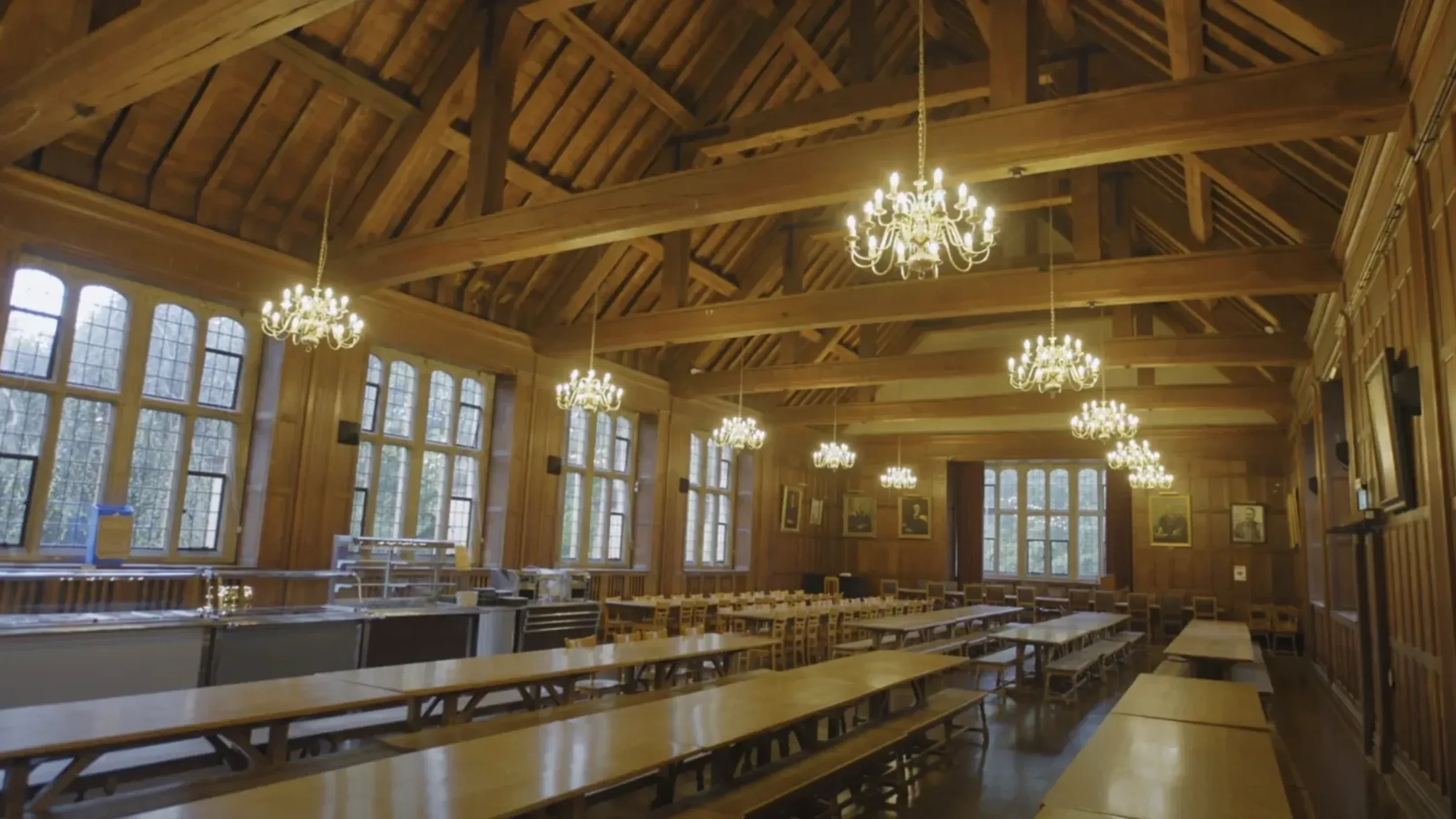 Wood-panelled dining hall with chandeliers and long tables at the University of Bristol.