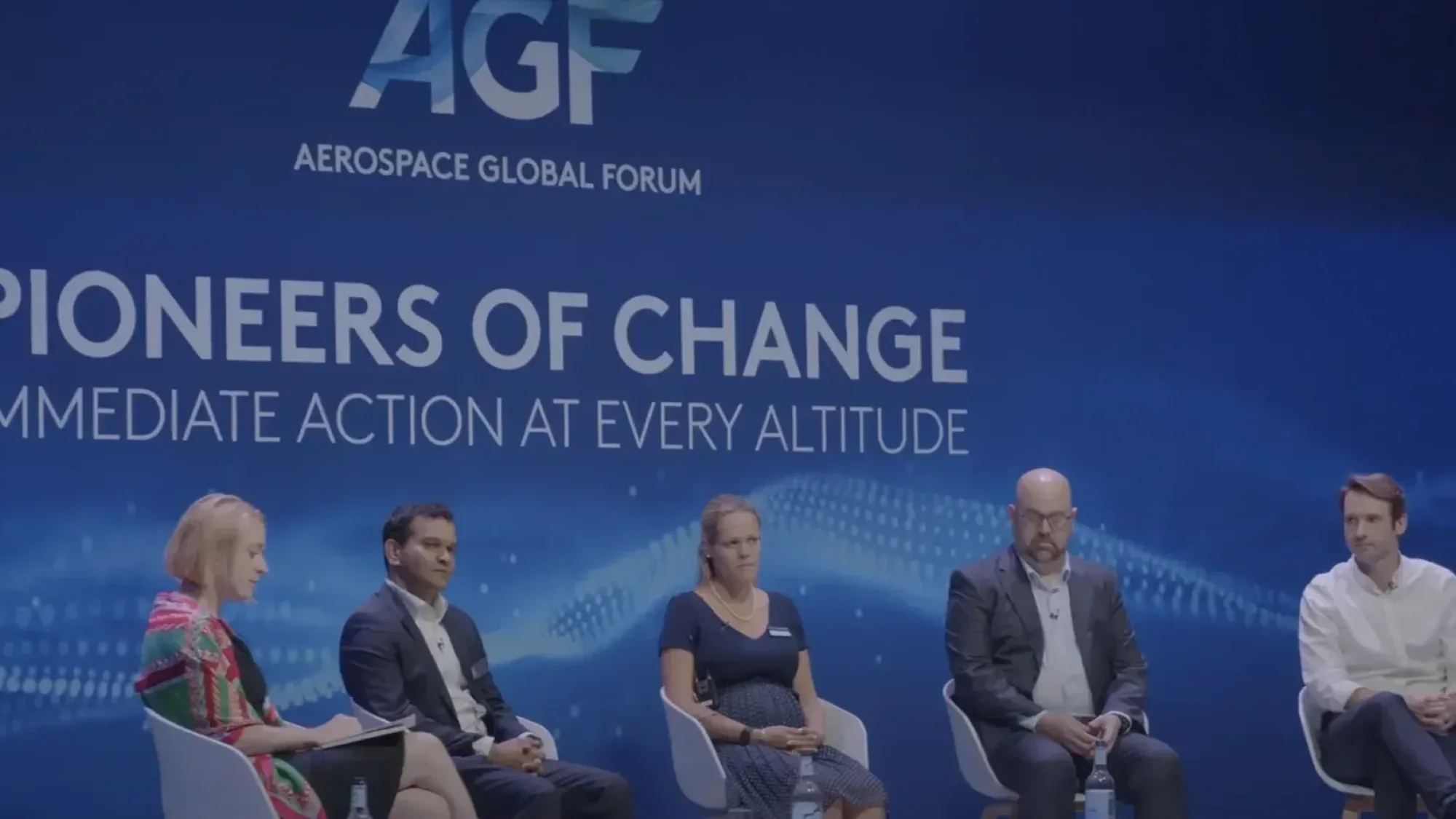 Panel of speakers sit on stage in front of a blue Aerospace Global Forum backdrop