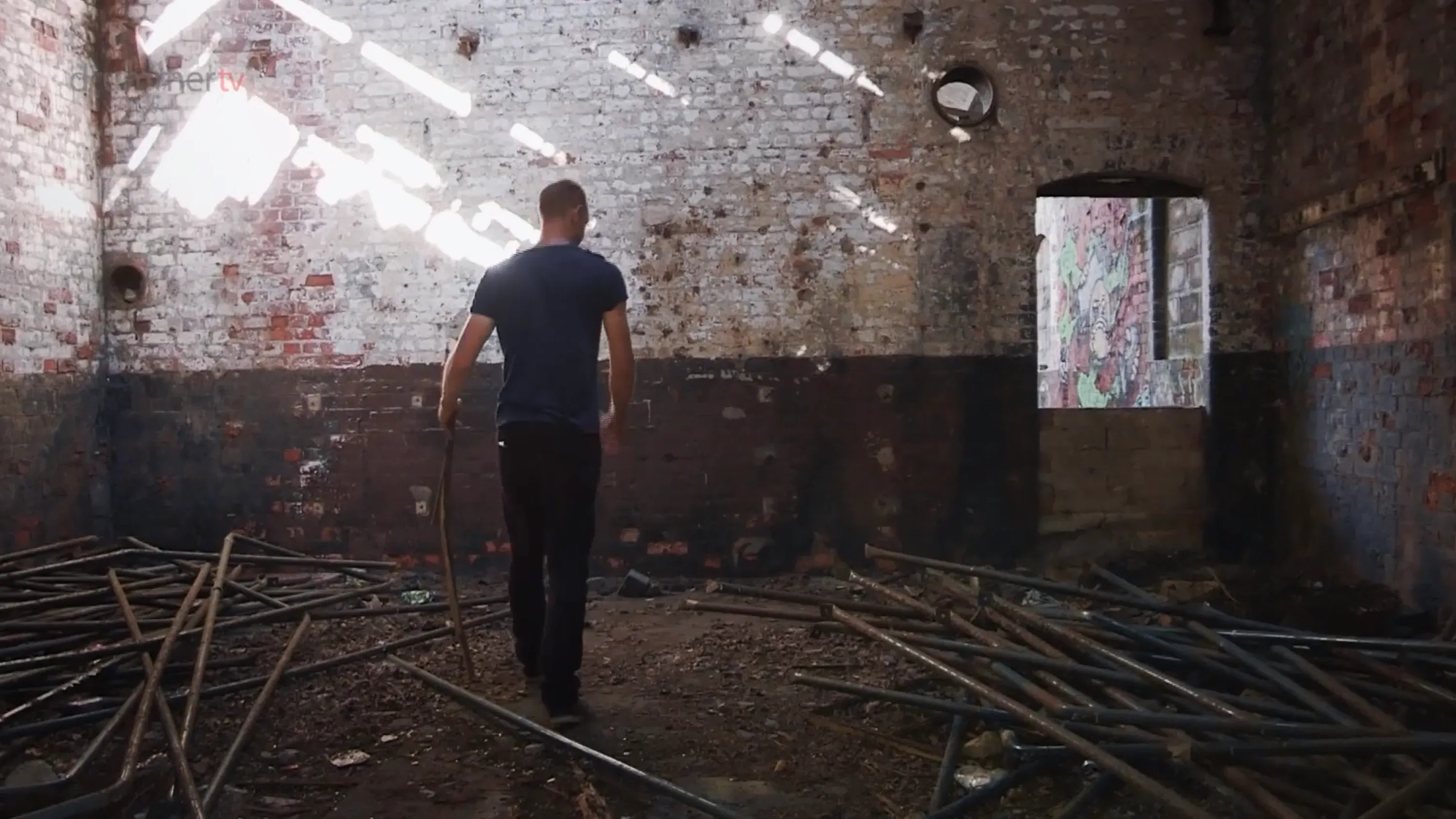 A man walks through a derelict brick building filled with scattered metal poles, filmed by Floating Harbour for the BBC Drama TV series Where Are You Sleeping Tonight.