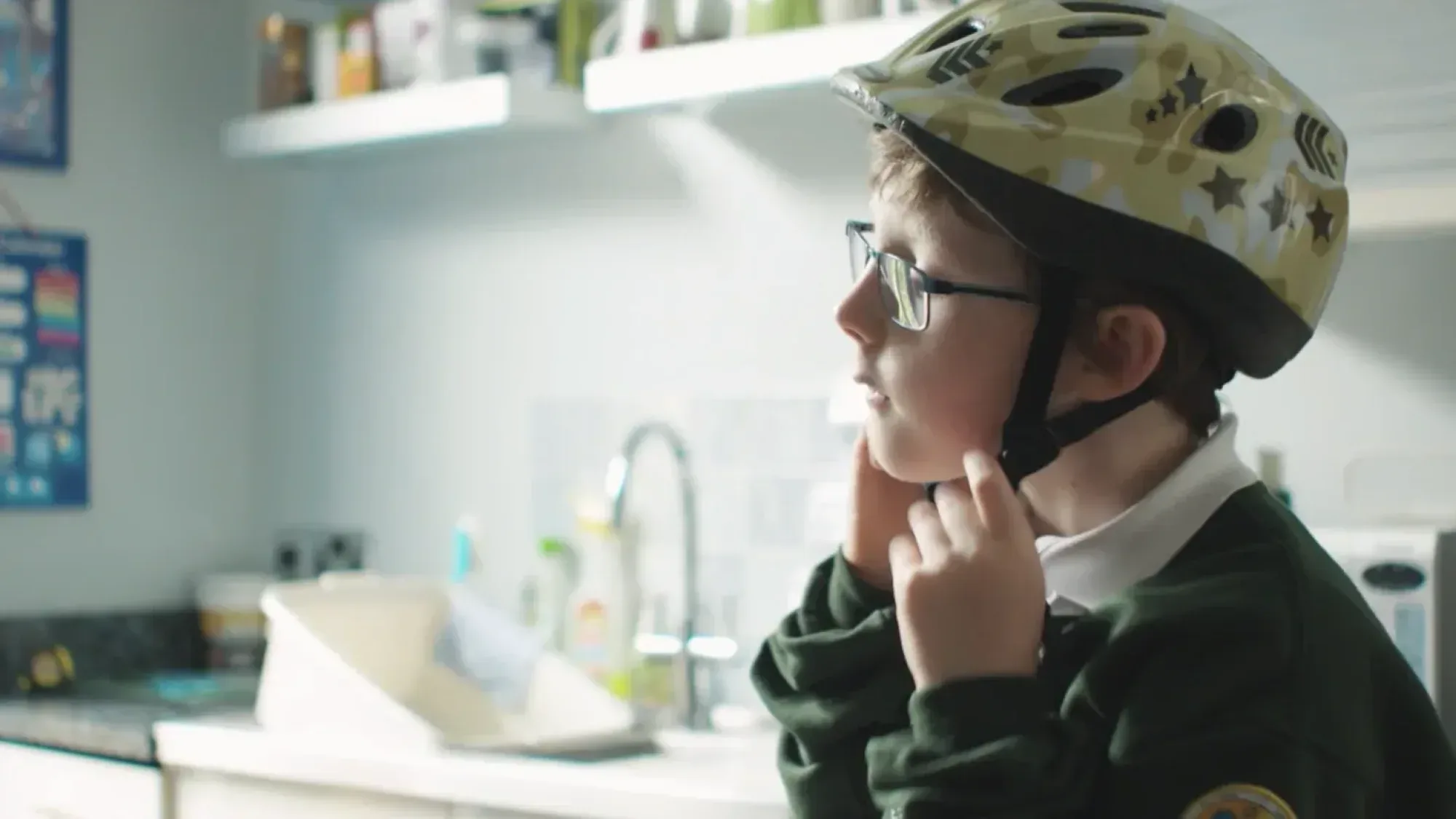 A child in school uniform fastens a patterned bike helmet in a kitchen for sustrans film