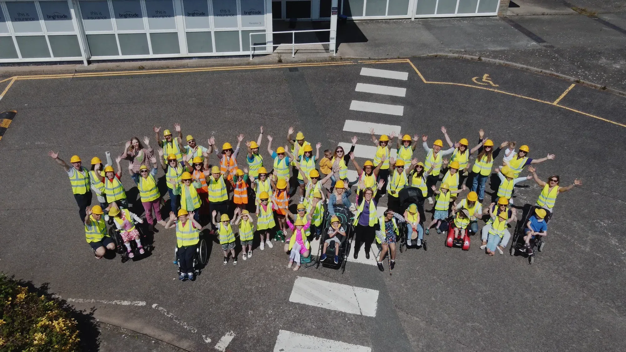 Group wearing high-visibility vests and hard hats waving at the camera during the Gympanzees site visit, photographed from above.