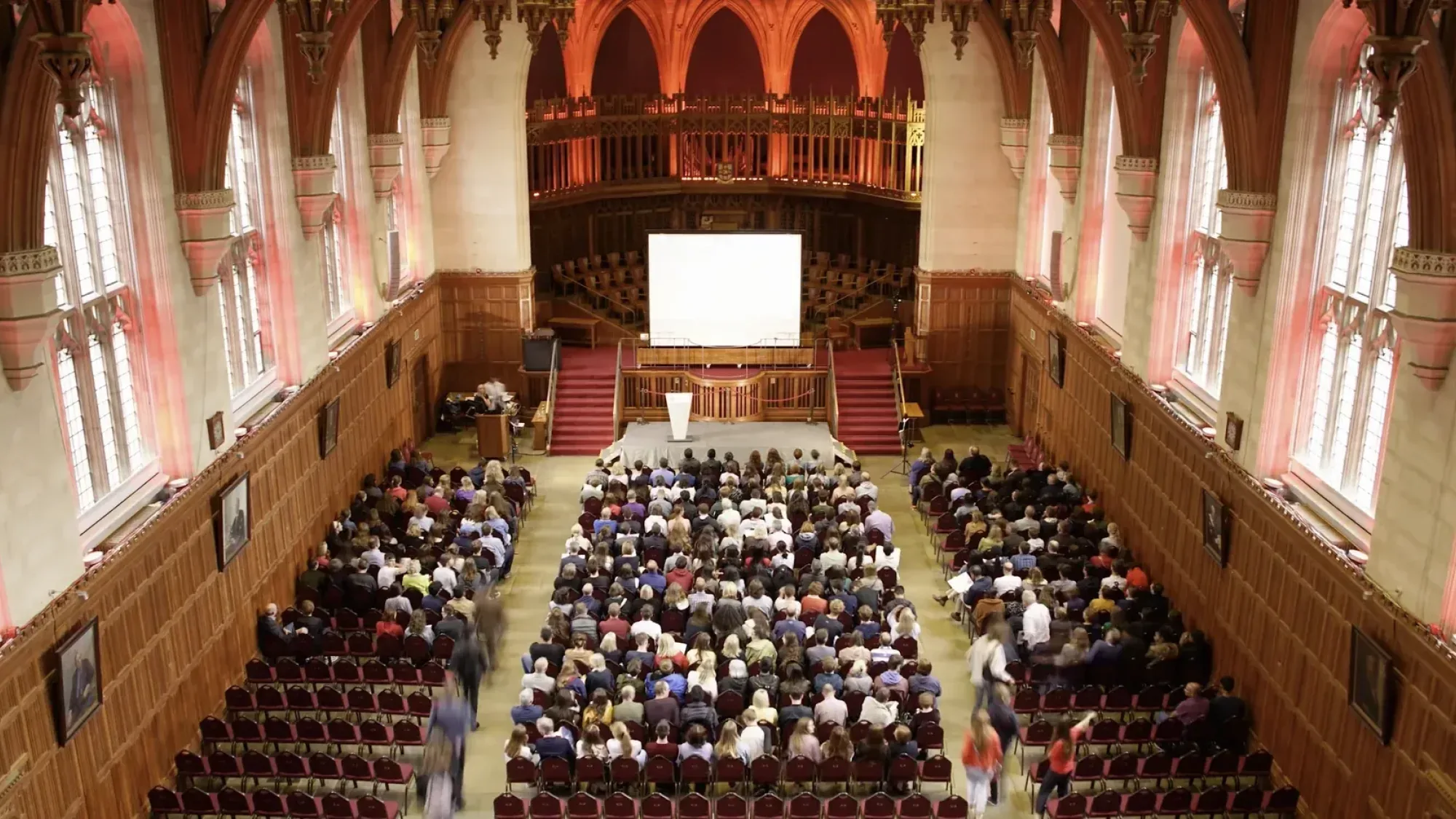 Large audience inside a grand hall at the University of Bristol watching a presentation on a central screen.