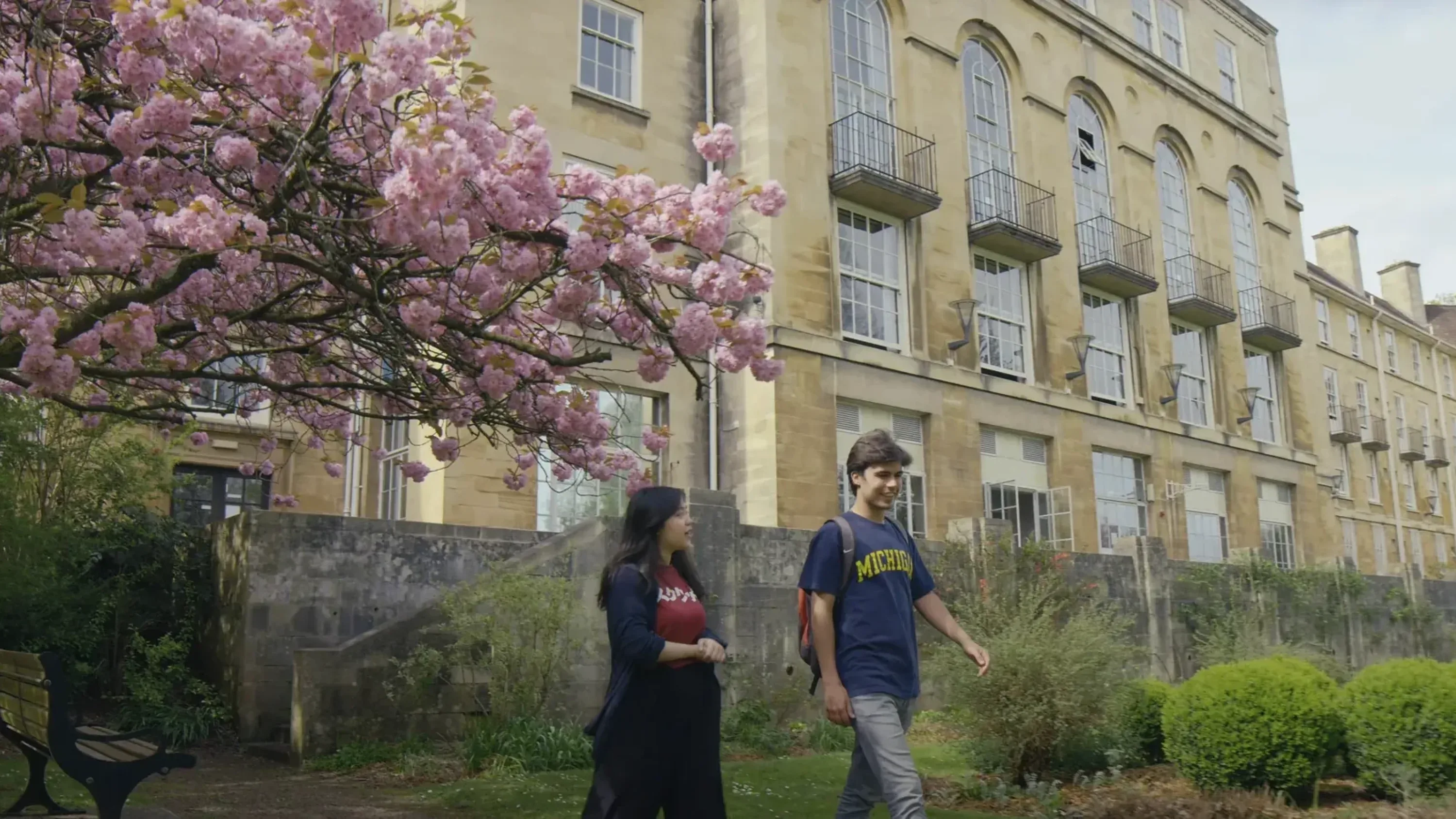 Two university students walking through the gardens at the University of Bristol beneath a flowering cherry tree.