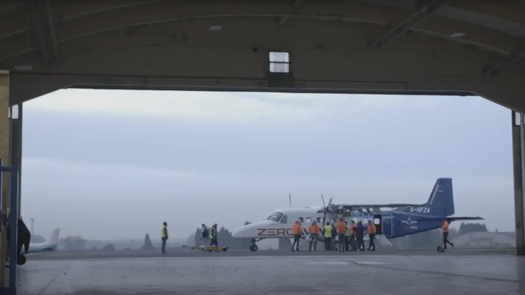 ZeroAvia hydrogen-electric Dornier 228 on the airfield apron with engineering crew preparing the aircraft for a test flight, seen from inside the hangar.